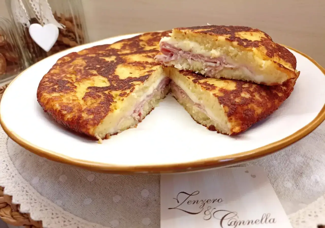 Focaccia di patate in padella con prosciutto cotto e formaggio filante, tagliata a met&agrave; per mostrare il ripieno goloso.