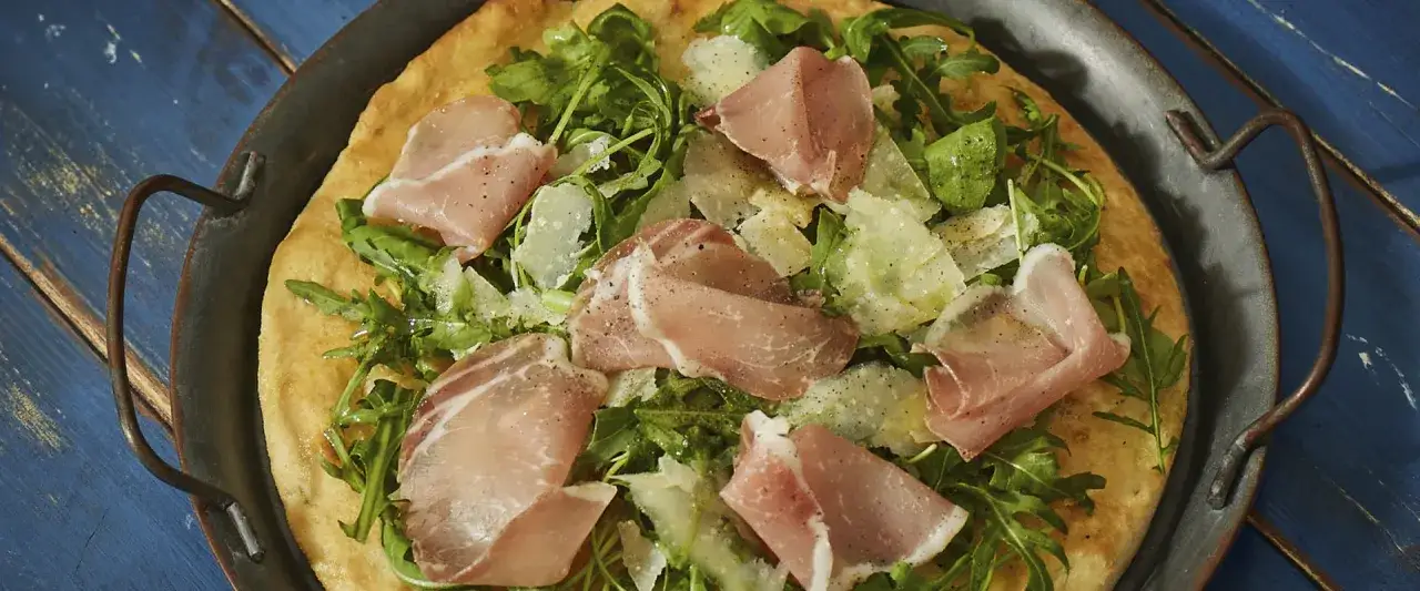 Pizza con bresaola, rucola fresca e scaglie di Grana Padano, condita con pepe nero. Un sapore italiano autentico.
