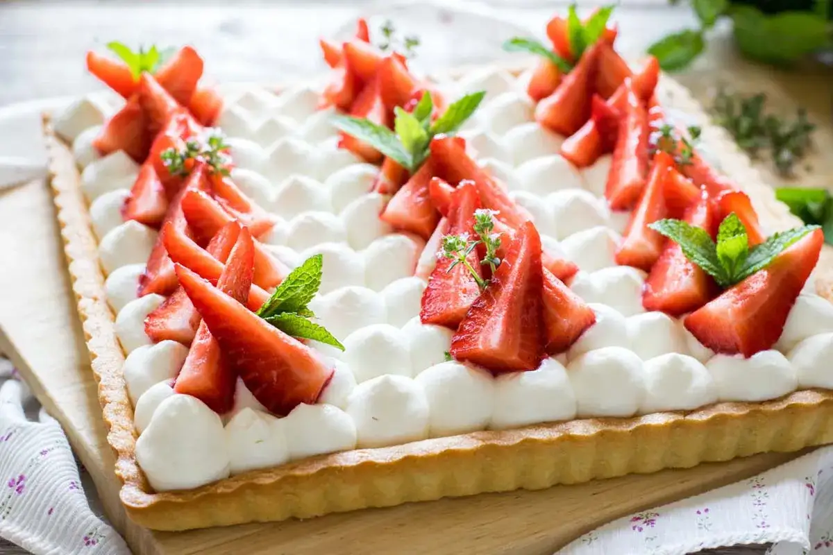 Crostata rettangolare con crema allo yogurt, fragole fresche a pezzi e foglie di menta.