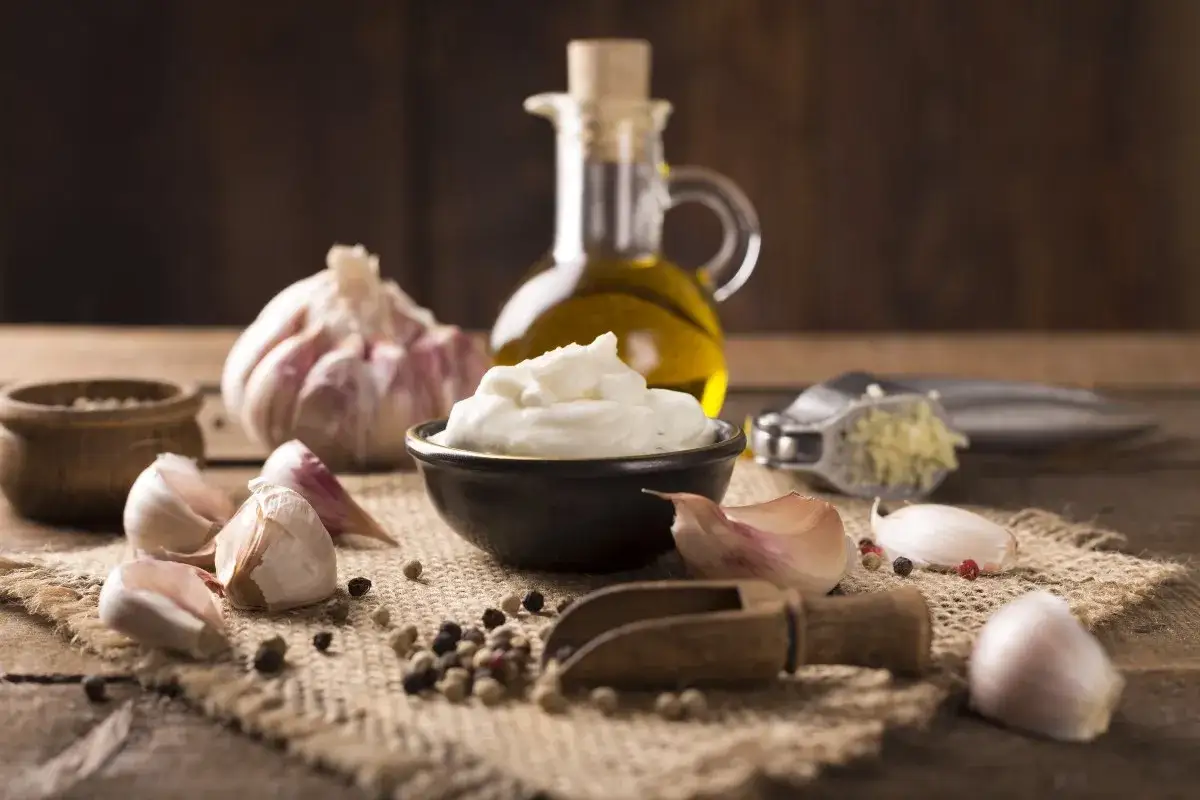 Ingredienti per un sos aioli: aglio, olio d'oliva, pepe e una ciotola di crema bianca.