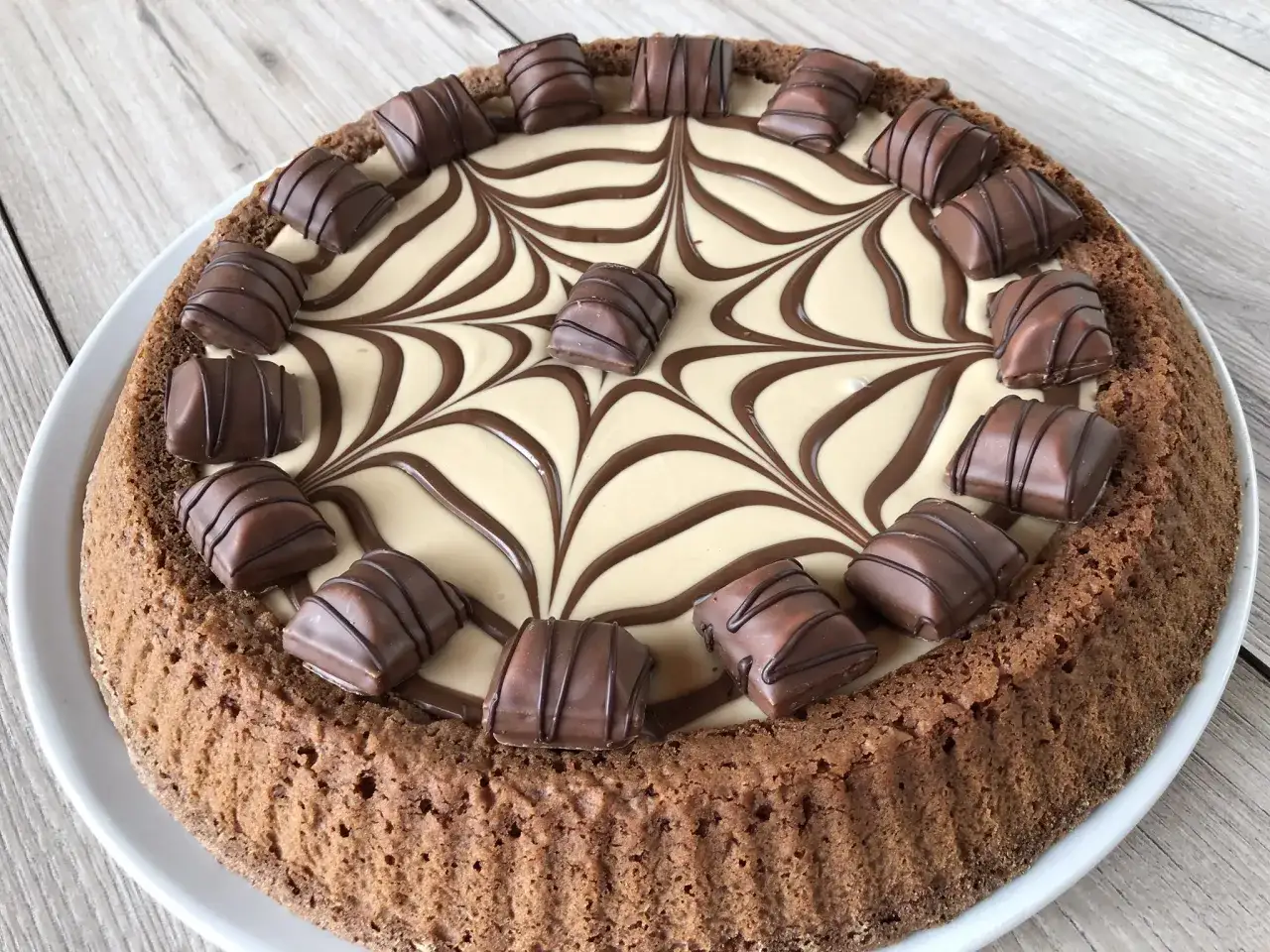 Torta con base croccante e crema chiara decorata con cioccolato, guarnita con pezzi di torta kinder bueno white.