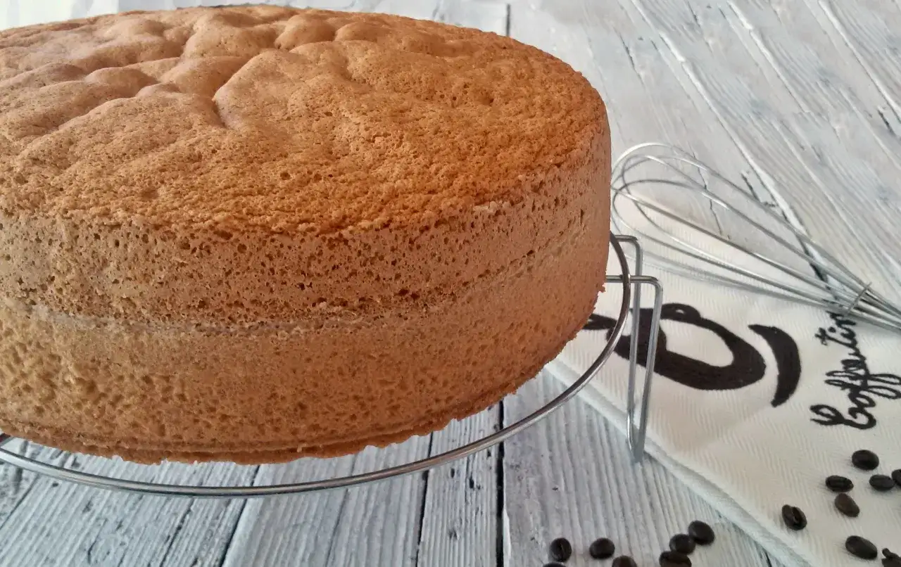 Una soffice base per torta, pronta per essere trasformata in una deliziosa bagna al caffè. Accanto, un frustino e chicchi di caffè.