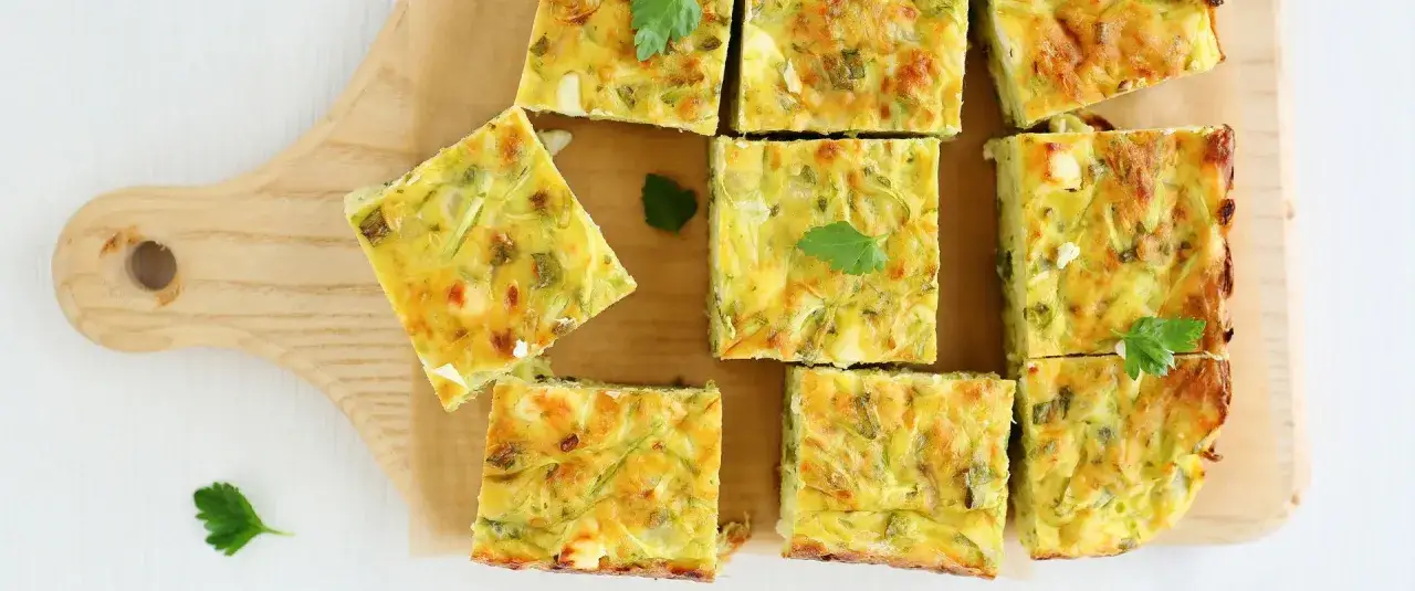 Fette di frittata con verdure miste, dorata e soffice, guarnita con prezzemolo fresco su tagliere di legno.