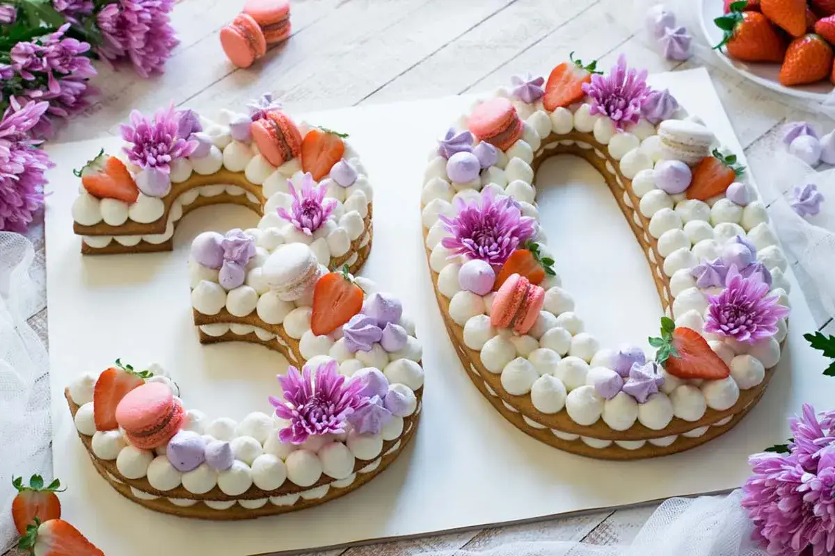 Una splendida torta numero 30, decorata con panna, fragole, macarons e fiori viola. Una ricetta torta numero perfetta per un compleanno speciale.