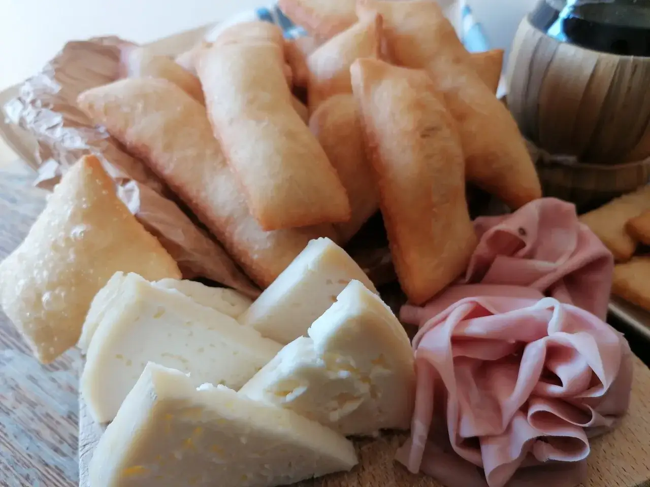 Sgabei fritti dorati e croccanti, accompagnati da formaggio fresco e fette di mortadella, un antipasto invitante.