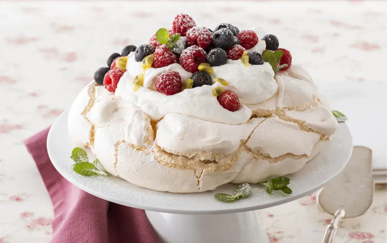 Un delizioso tort pavlova con panna montata, lamponi, mirtilli e semi di frutto della passione, guarnito con menta fresca.