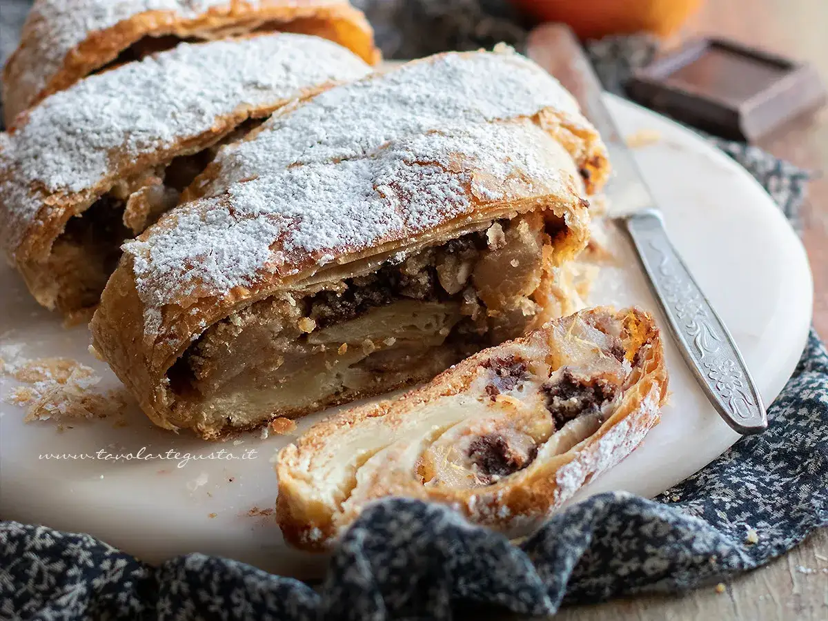 Strudel pere cioccolato e amaretti, una delizia dorata cosparsa di zucchero a velo, con un ripieno invitante.