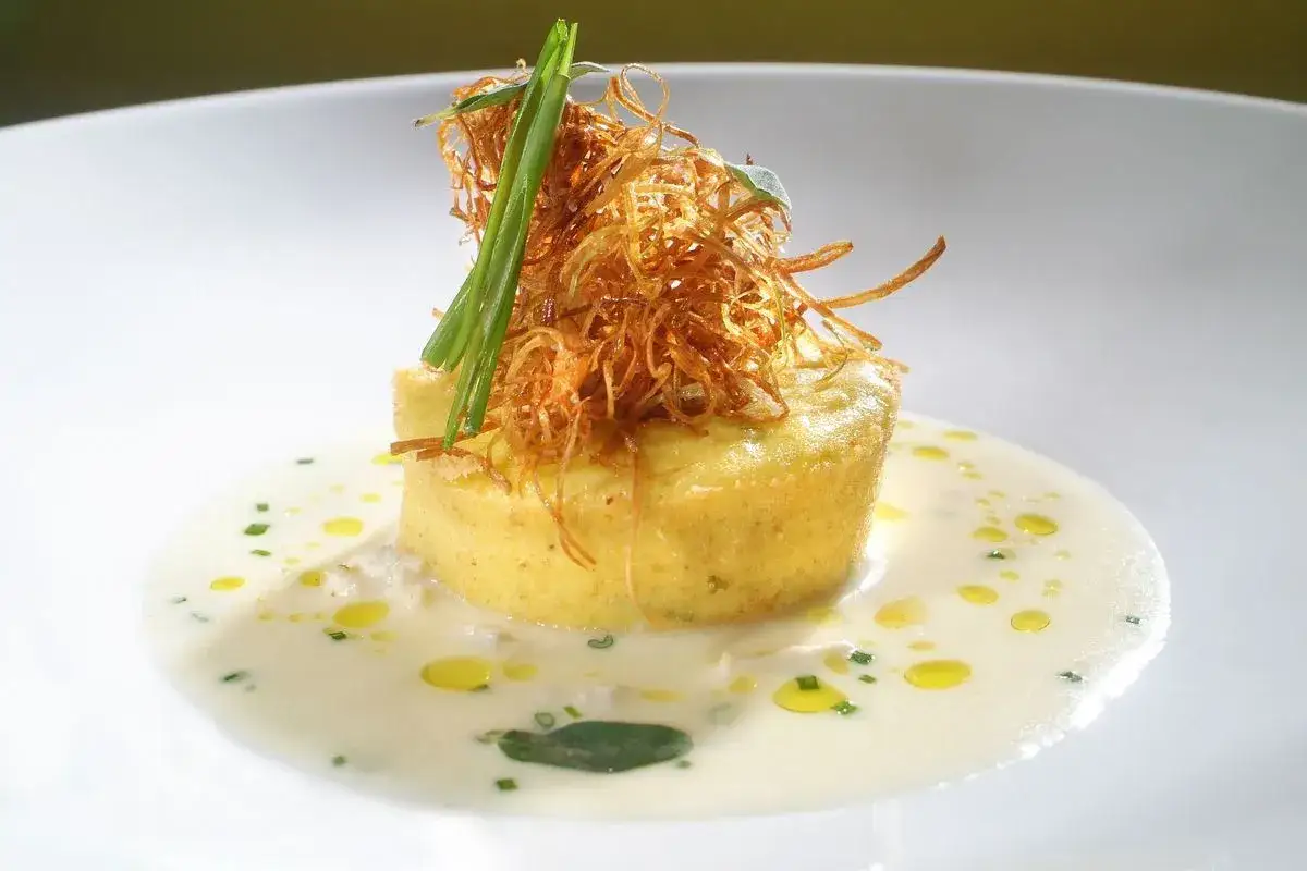 Flan di porri con salsa di acciughe, guarnito con cipolla croccante e erbe aromatiche. Un piatto raffinato che celebra i sapori del mare e della terra.