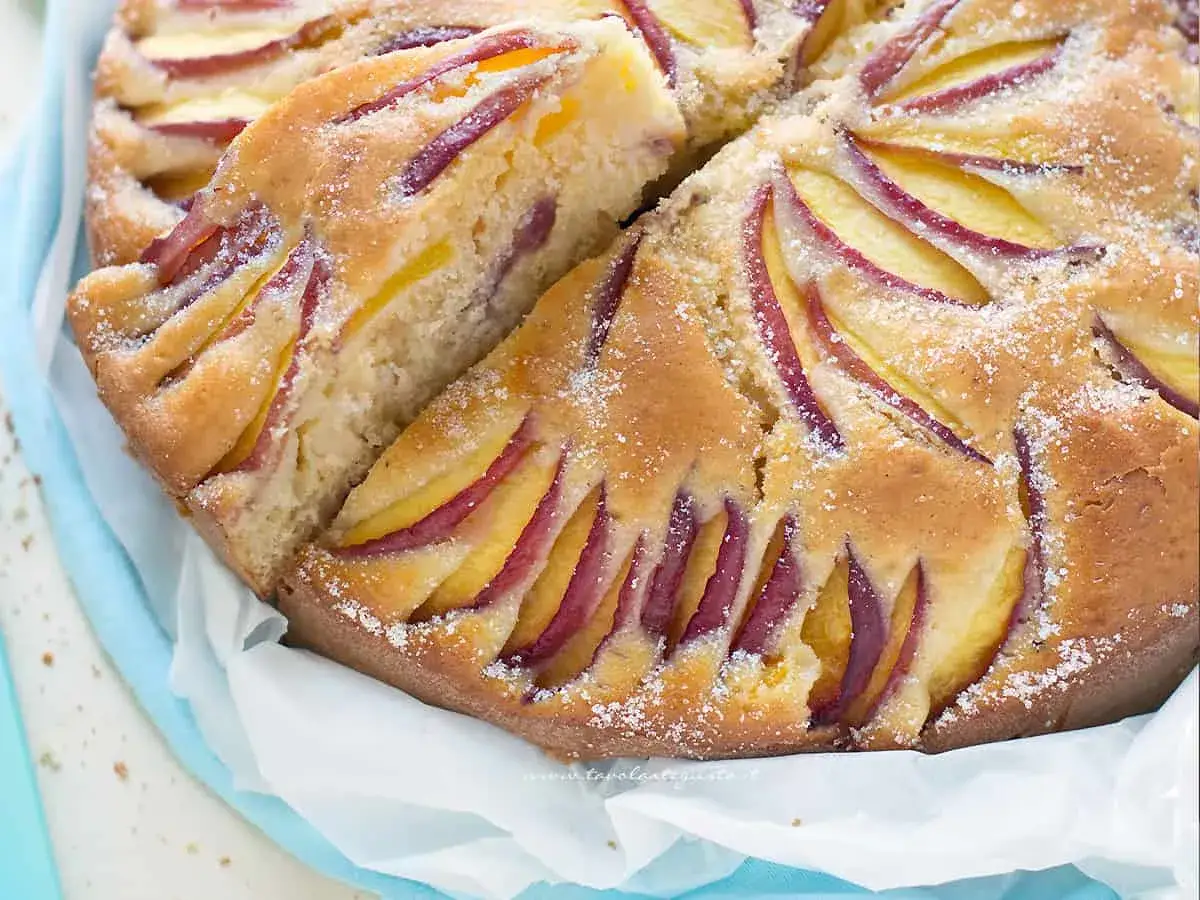 Delizioso ciasto z brzoskwiniami, con fette di frutta succosa incastonate in una soffice torta dorata, cosparsa di zucchero.