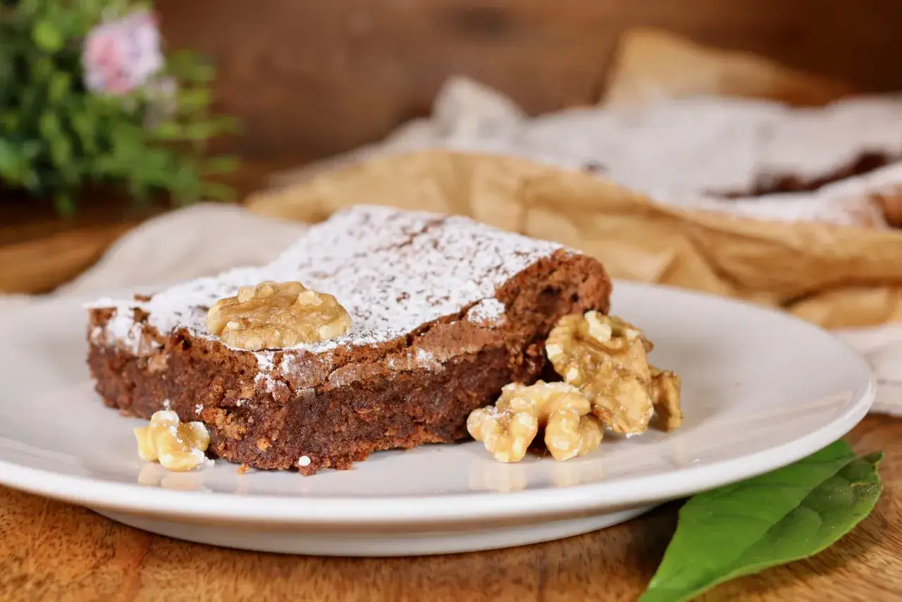 Una fetta di torta noci e cioccolato senza farina, spolverata di zucchero a velo e guarnita con noci intere e spezzate.