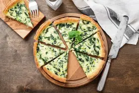 Torta salata spinaci e mozzarella, con un tocco di speck affumicato, tagliata a spicchi su un tagliere di legno.