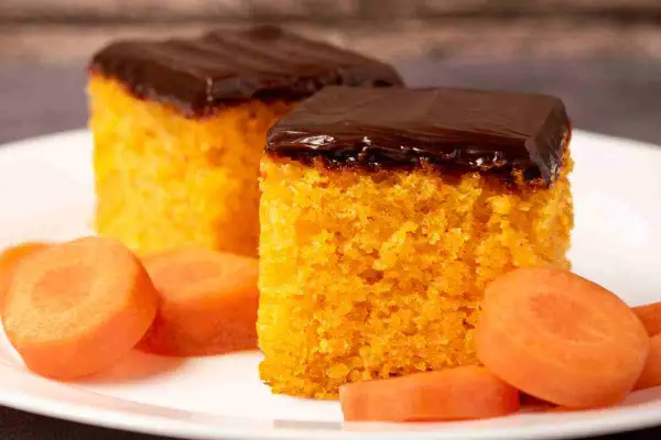 Due fette di ciasto marchewkowe, soffice e arancione, ricoperte di glassa al cioccolato fondente, con fettine di carota fresca intorno.