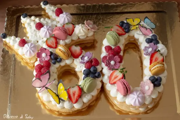Una torta numero 60 decorata con panna, frutta fresca, macarons e farfalle. Una deliziosa ricetta torta numero per festeggiare.