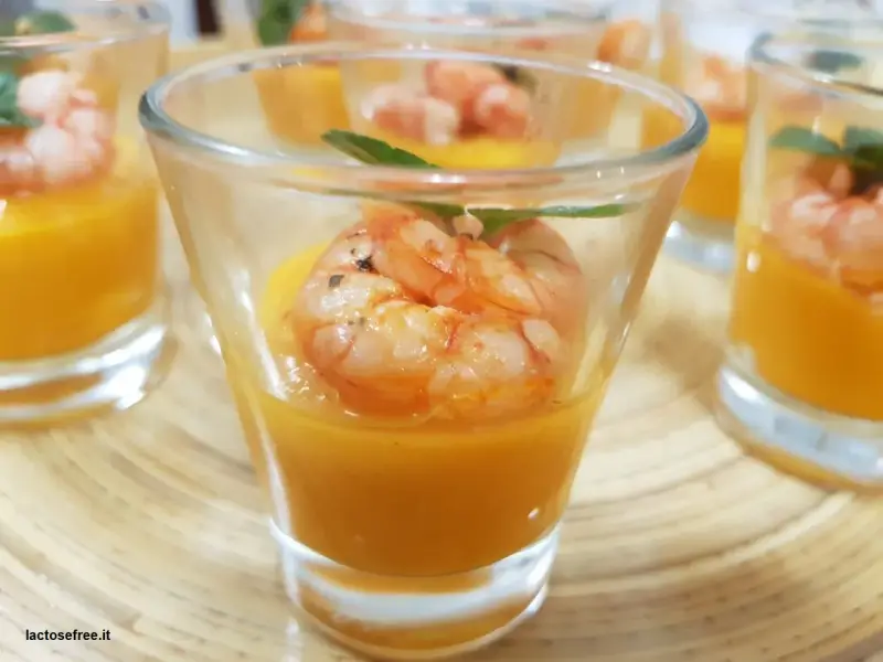 Deliziosi gamberi aperitivo in bicchierini con crema arancione e foglioline verdi.
