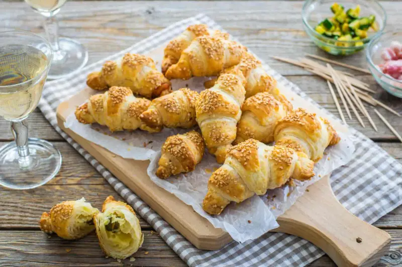 Croissant dorati con ripieno di pasta sfoglia e semi di sesamo, pronti per essere gustati con un bicchiere di vino.
