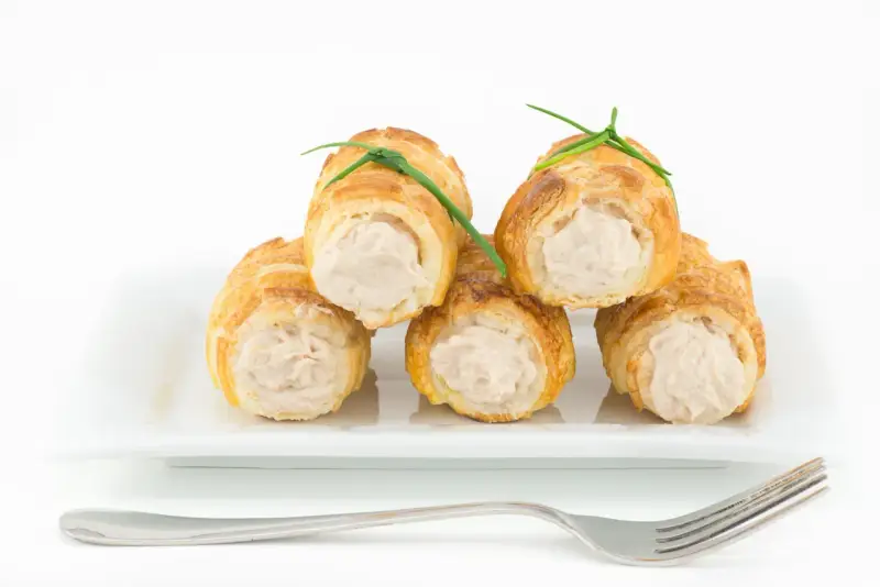 Cannoli salati ripieni di tonno, guarniti con erba cipollina, su un piatto bianco con forchetta.