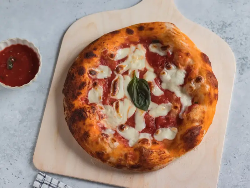 Pizza napoletana appena sfornata, con pomodoro, mozzarella filante e basilico fresco, pronta per essere gustata.