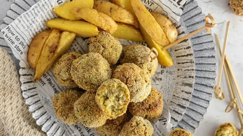 Polpette di verza e ricotta dorate e croccanti, servite con spicchi di patate fritte su carta di giornale.